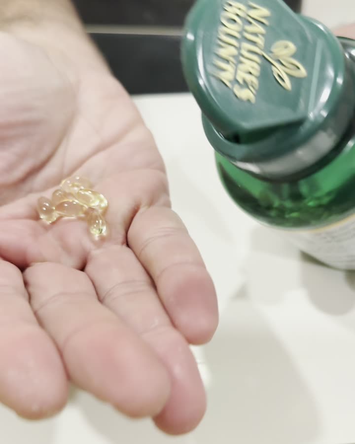 A palm holding about ten vitamin D softgels tipped from an open bottle.