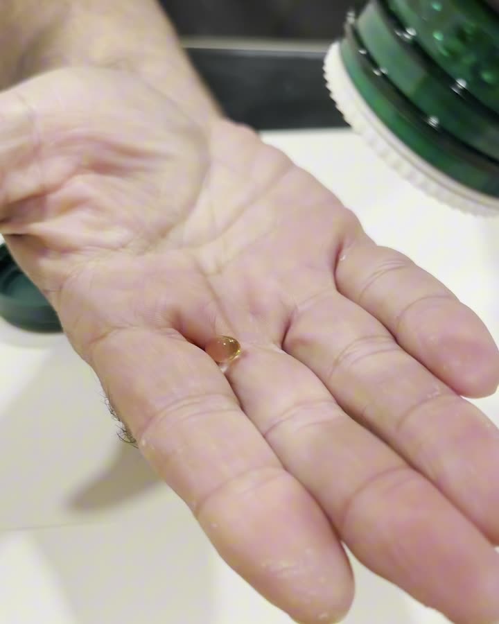 A palm holding a single vitamin D softgel.